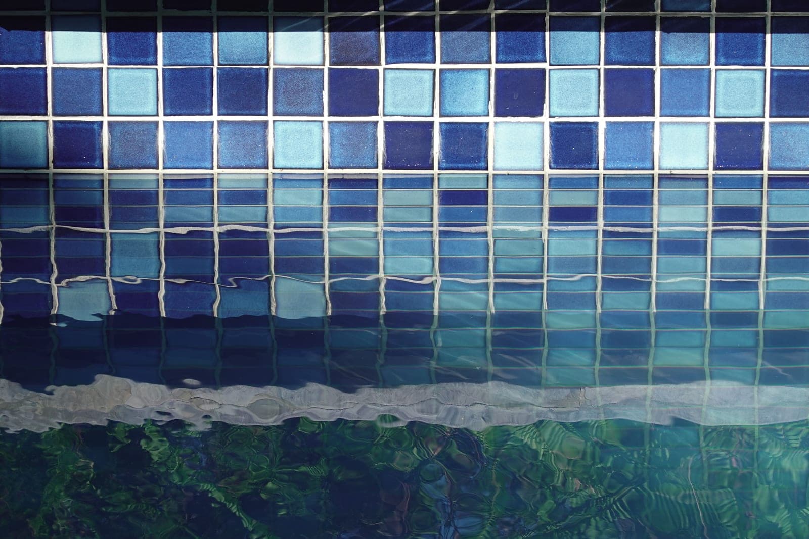 The tiled edge of a swimming pool at dusk with still, clear water